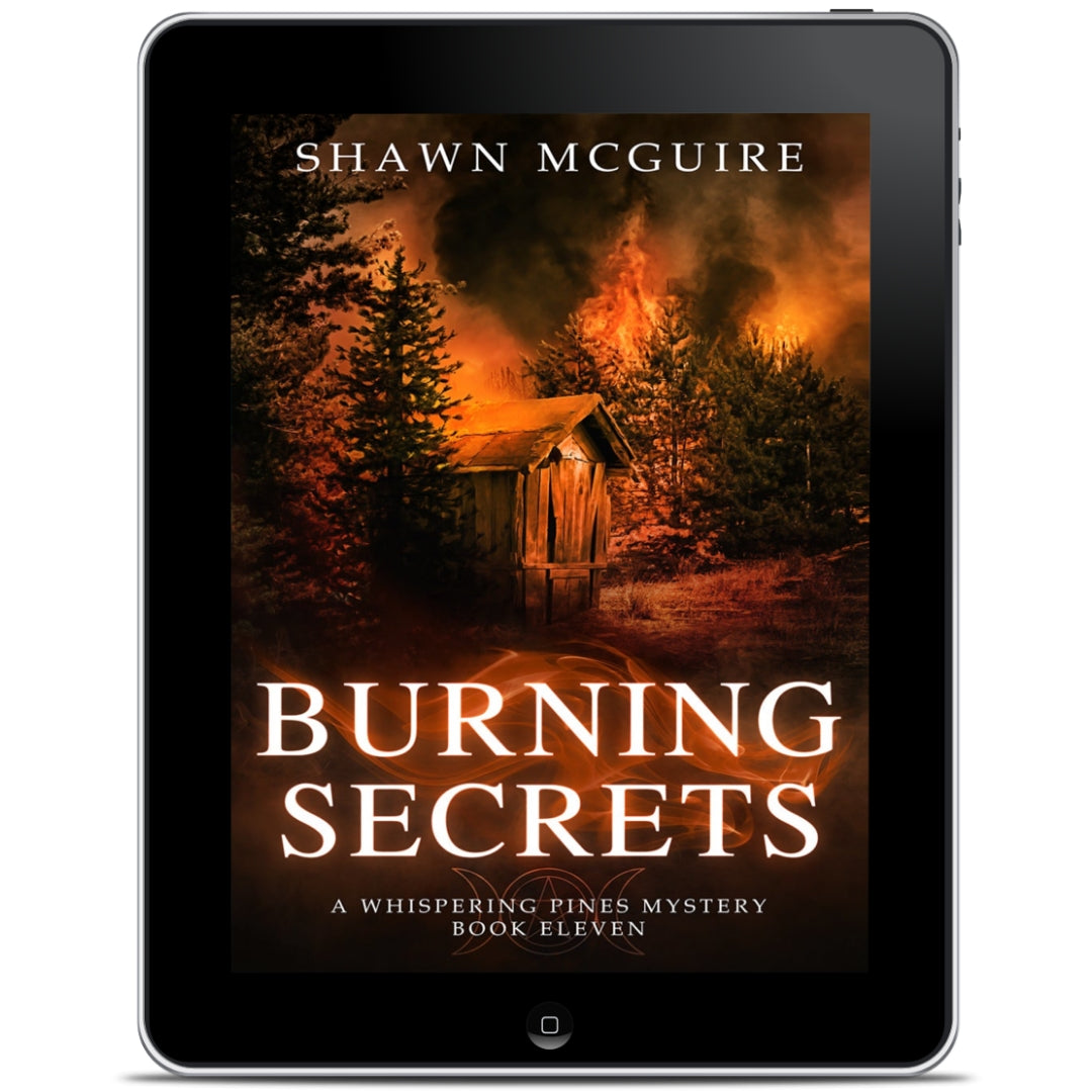 E-book cover on e-reader of Shawn McGuire's cozy murder mystery set in Whispering Pines, featuring a burning forest and shack.